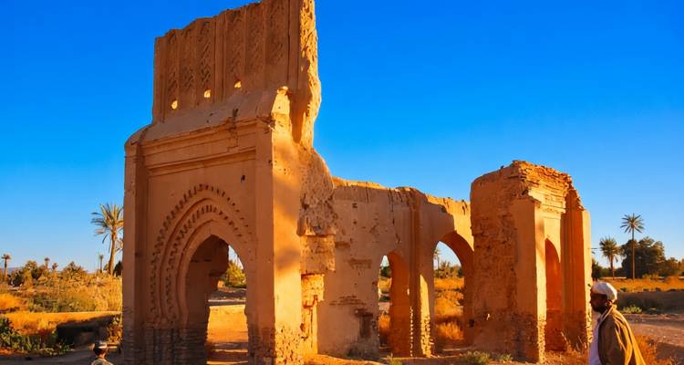 Un homme solitaire passe devant des ruines d'adobe ensoleillées et des palmiers sous un ciel bleu éclatant.
