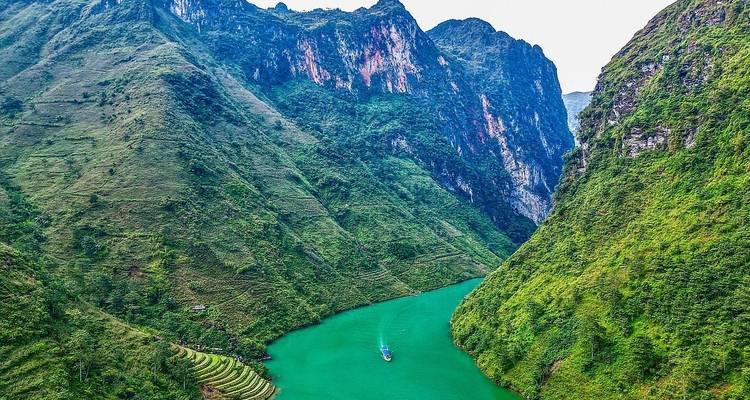 Lebendige Luftaufnahme eines schmalen jadegrünen Flusses, der sich zwischen hohen grünen Bergen in Nordvietnam schlängelt.