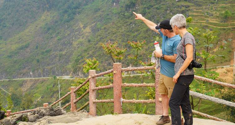 Ein reisendes Paar betrachtet die ferne Berglandschaft von einem rustikalen Aussichtspunkt-Geländer.
