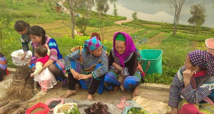 Colorfully dressed ethnic women and children selling produce at an open-air market by a river