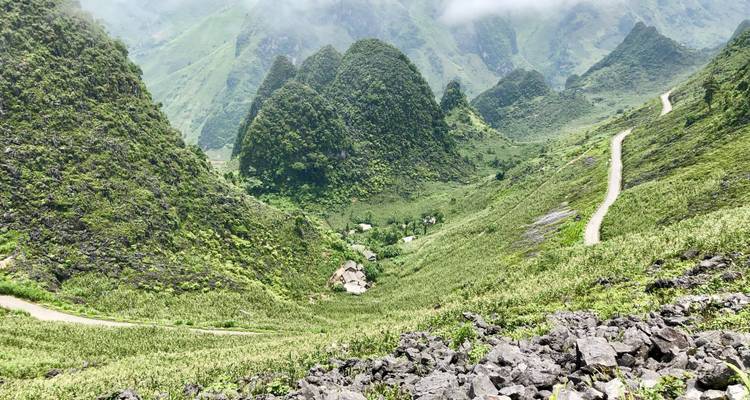 Karstspitzen und felsige Hänge, die in ein tiefgrünes Tal mit einem schmalen Pfad abfallen