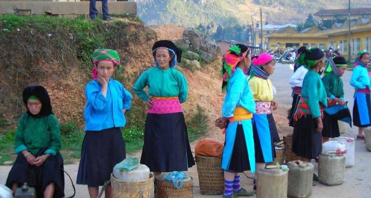 Vrouwen in kleurrijke traditionele kledij staan met manden en containers op een plattelandsmarkt.