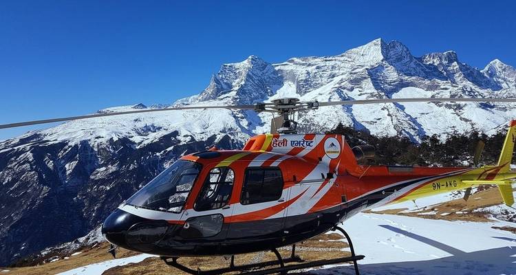 Helicopter parked on snowy terrain with mountain backdrop.