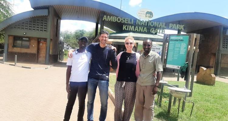Quatre voyageurs posent ensemble devant le bâtiment d'entrée de la porte Kimana du parc national d'Amboseli par une journée ensoleillée.
