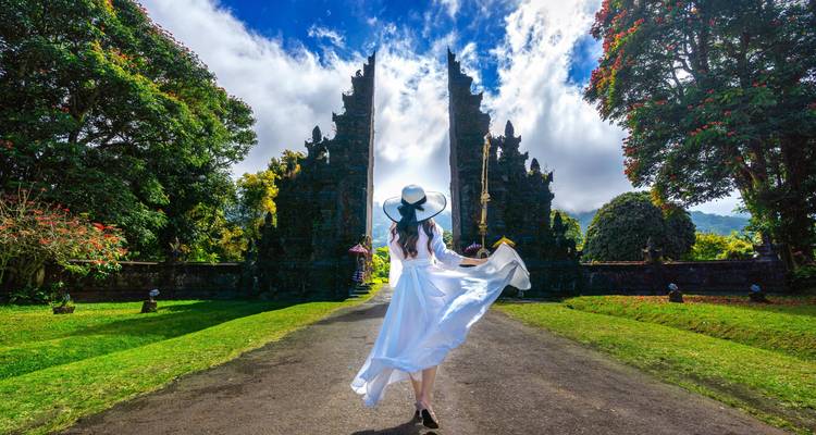 Mujer en un vestido blanco caminando hacia una puerta tradicional.