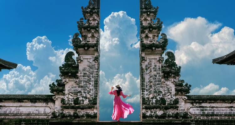 Mujer con vestido rojo posando en una puerta tradicional balinesa.