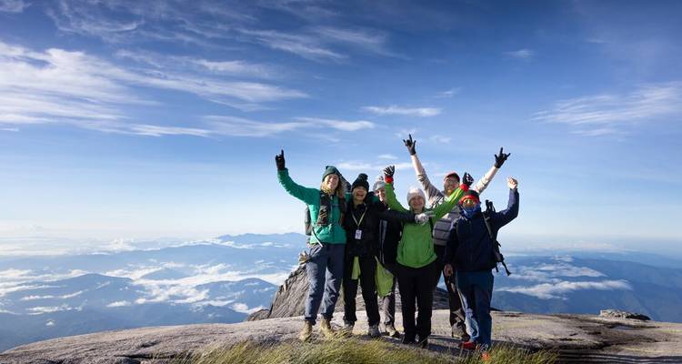Overwinnaars van de tocht vieren op de rotsachtige top van Mount Kinabalu boven een zee van wolken.