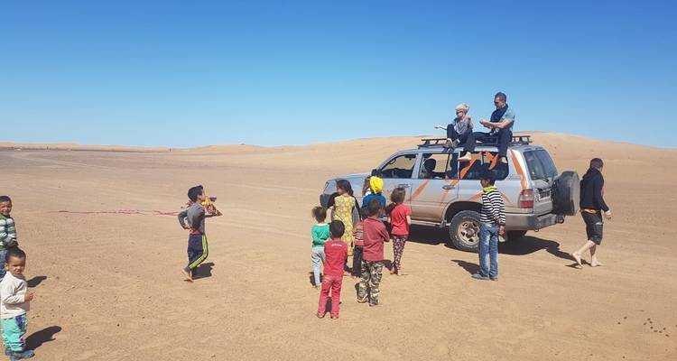 Des enfants rassemblés autour d'un véhicule dans un désert.