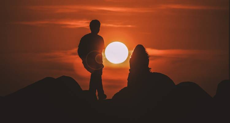Silhouette of two people at sunset with the sun in the background.