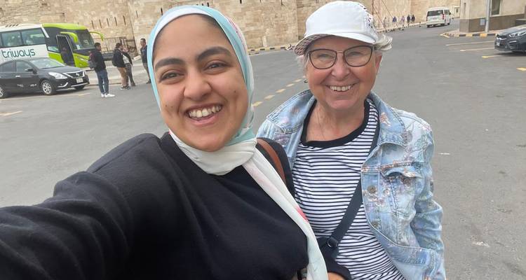 Zwei Frauen, die in einem Selfie lächeln, mit historischen Steinmauern und geparkten Reisebussen im Hintergrund