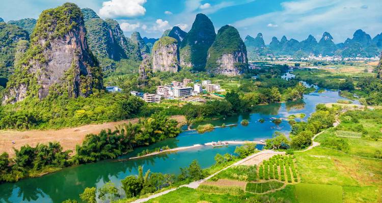 Luchtfoto van smaragdgroene rivieren, rijstvelden en imposante kalksteenpieken onder een stralend blauwe hemel van Guilin.