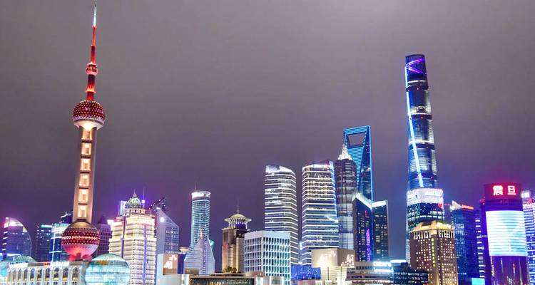 Shanghai skyline 's nachts met verlichte wolkenkrabbers inclusief de Oriental Pearl Tower onder een bewolkte hemel.
