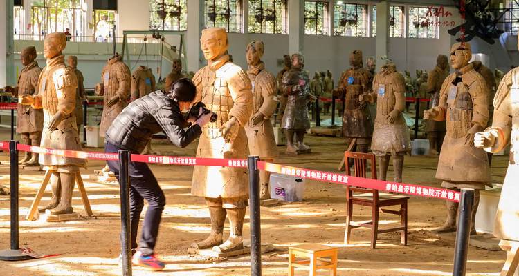 Fotograaf hurkt neer om close-upfoto's te maken van een terracotta krijger in een open restauratiehangaar.