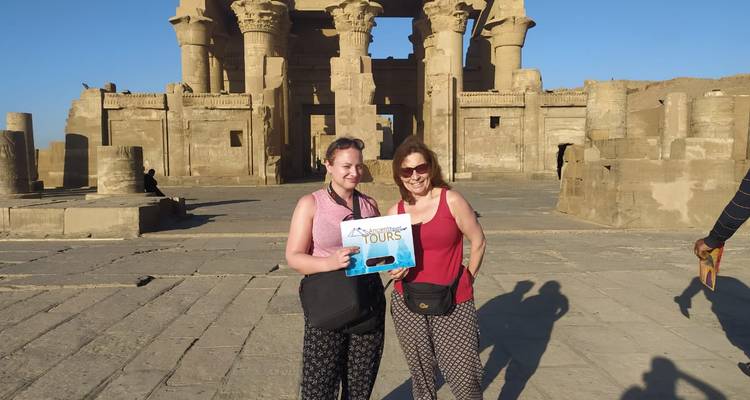 Two tourists holding a sign in front of an ancient temple.