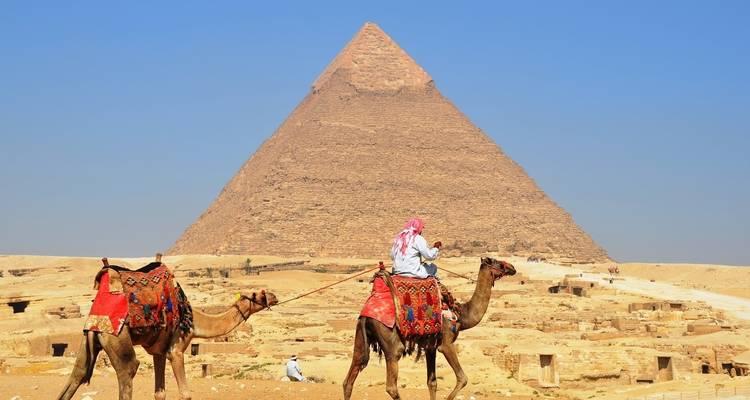 Pyramid with camels and riders in the foreground.