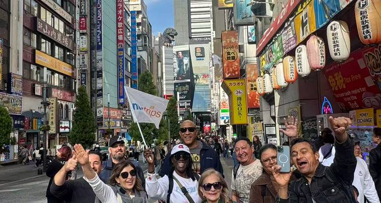 Große Reisegruppe jubelt auf einer belebten Straße in Tokio mit dem Godzilla-Kopf, der im Hintergrund aufragt