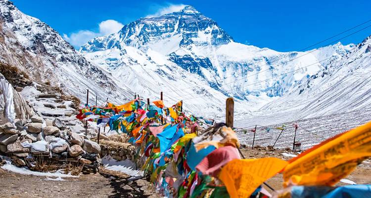 Leuchtende Gebetsfahnen flattern im Vordergrund, während das majestätische, schneebedeckte Nordgesicht des Mount Everest dahinter aufragt.
