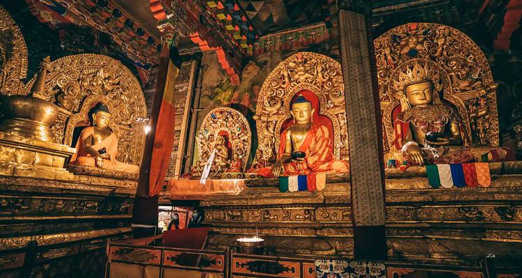 Goldene Buddhafiguren und bunte Wandmalereien säumen das reich verzierte Innere einer tibetischen Klosterhalle.