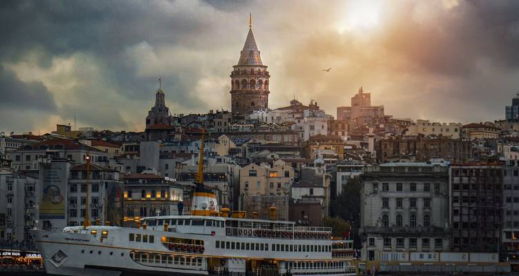 Galata Tower with a ferry in the foreground at sunset.