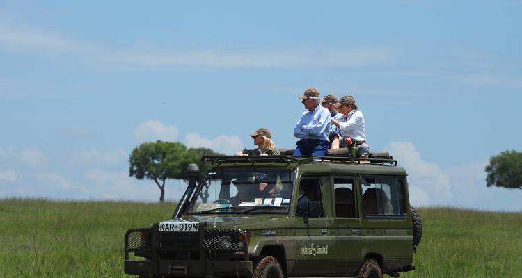 Gruppe von Touristen in einem Safari-Fahrzeug in einer Savanne.