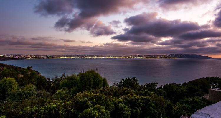 Vue sereine de l'océan au crépuscule avec les lumières de la ville au loin.