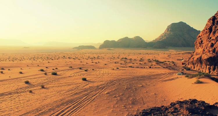 Wüstenlandschaft mit rötlichem Sand und fernen Felsformationen.