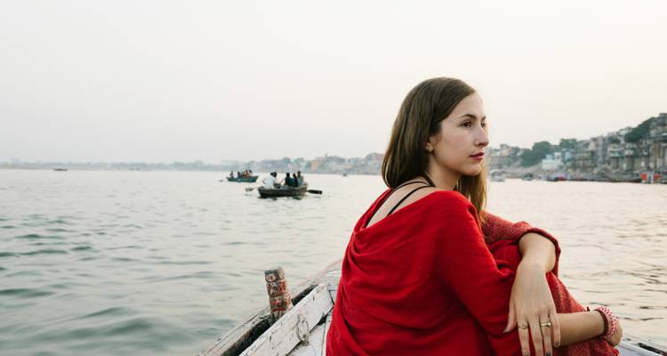 Frau, die auf einem Boot auf dem Fluss sitzt, mit einer Stadtsilhouette im Hintergrund.