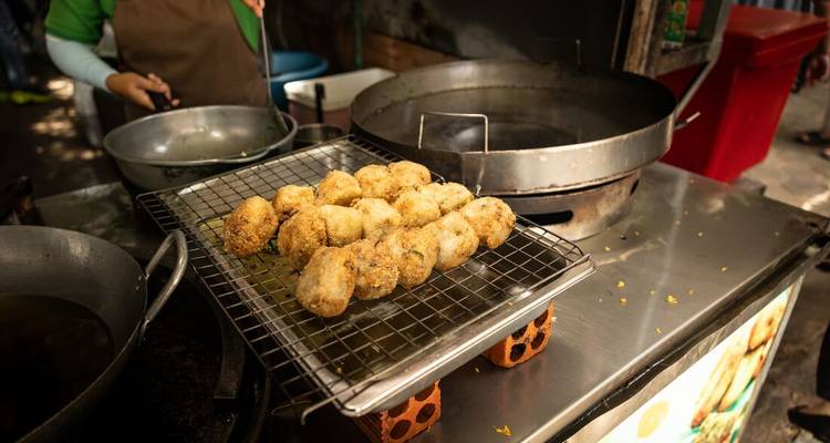Des collations de rue fraîchement frites refroidissent sur une grille dans une échoppe alimentaire cambodgienne animée.