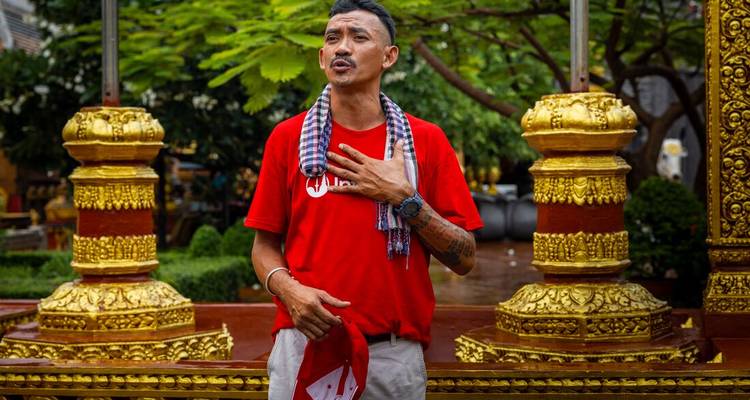 Un guide local en chemise rouge parle avec passion devant des colonnes de temple dorées ornementées.