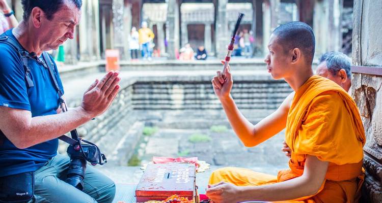 Un moine bouddhiste bénit un photographe de passage à l'intérieur d'un ancien temple de pierre.