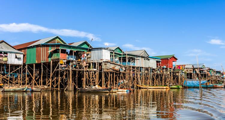 Des maisons sur pilotis colorées s'élèvent au-dessus de l'eau réfléchissante du lac Tonlé Sap sous un ciel dégagé.