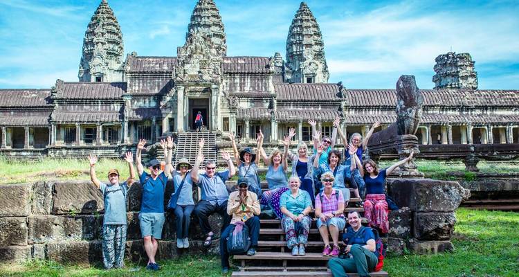Un groupe de touristes pose les mains levées sur les marches de la façade emblématique d'Angkor Vat.