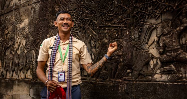 Un guide joyeux explique les sculptures complexes en bas-relief sur un mur de temple d'Angkor.