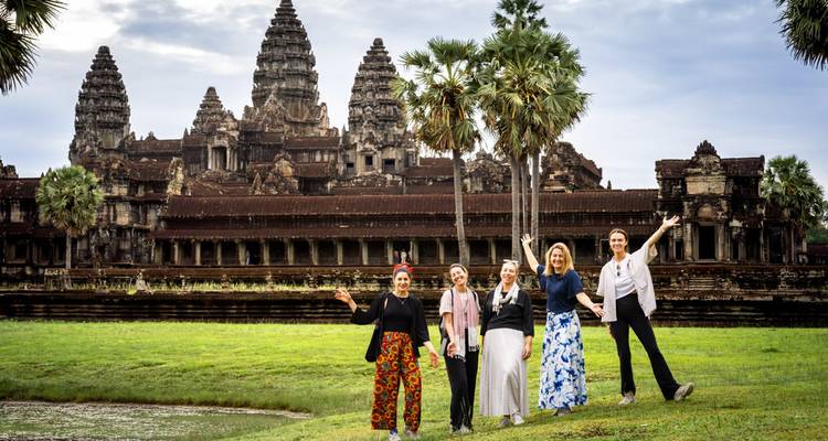 Cinq voyageurs posent joyeusement devant les tours d'Angkor Wat de l'autre côté d'un fossé verdoyant.