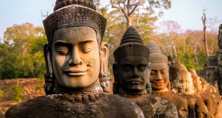 Statues de pierre de divinités alignées avec des arbres en arrière-plan.