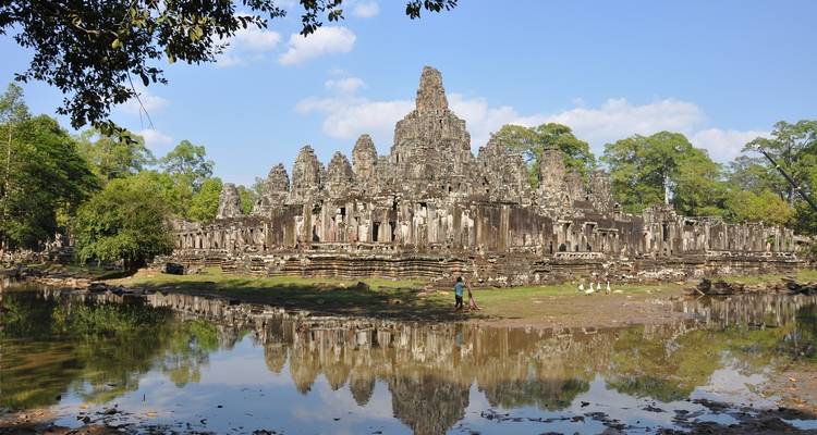 Ruines de temple se reflétant dans un plan d'eau entouré d'arbres.