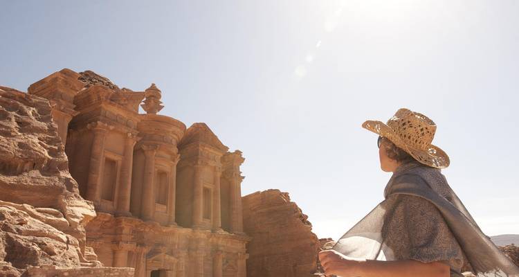 Eine Person mit einem Strohhut bewundert die antike, in Fels gehauene Architektur von Petra.