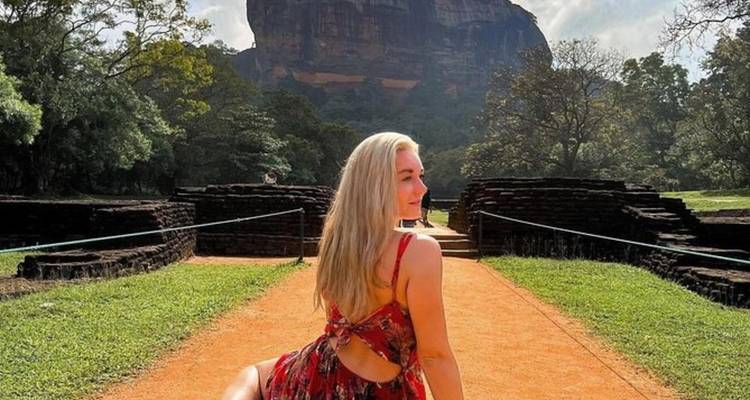 A woman posing in front of a rock fortress with expansive views.