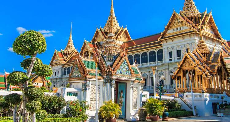 Grand Palace complex in Bangkok with ornate golden spires under a brilliant blue sky