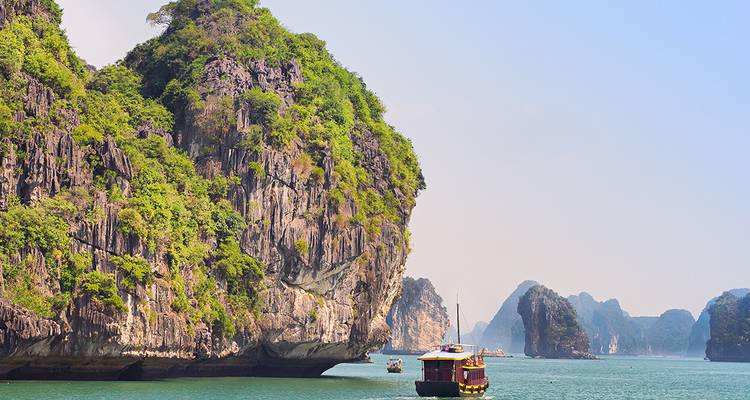 Wooden junk boat cruising between towering limestone karsts in Ha Long Bay