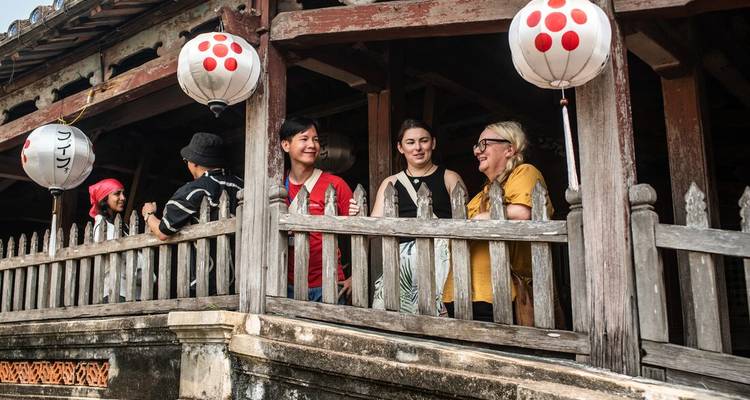 Smiling travellers stand on the historic wooden Japanese Covered Bridge decorated with lanterns.