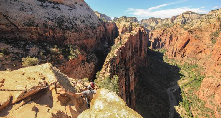 Un randonneur grimpe un sentier de crête équipé de chaînes surplombant un profond canyon