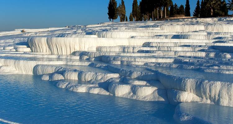 Witte travertijn terrassen van Pamukkale die blauw water reflecteren.