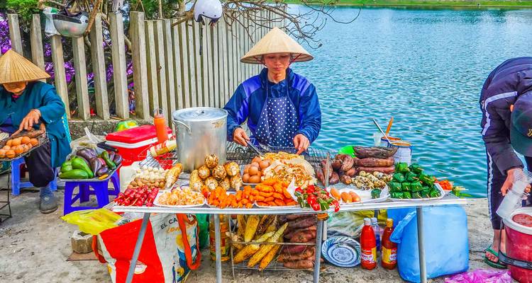 Straatvoedselverkoper die verschillende snacks bereidt bij een rivier.