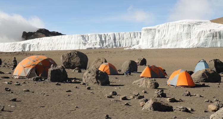 Camping tents set amidst rocky terrain with a glacier in the background.