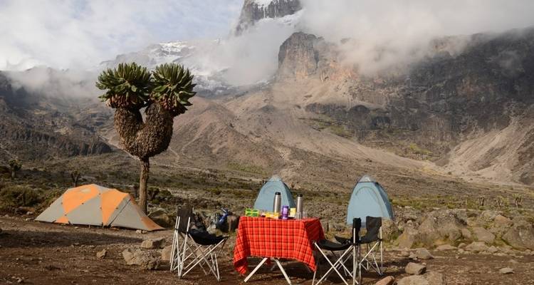 Camp site with tents and a table set in a mountainous terrain.