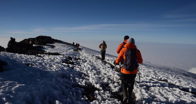 Hikers walking on a snowy trail at high altitude.