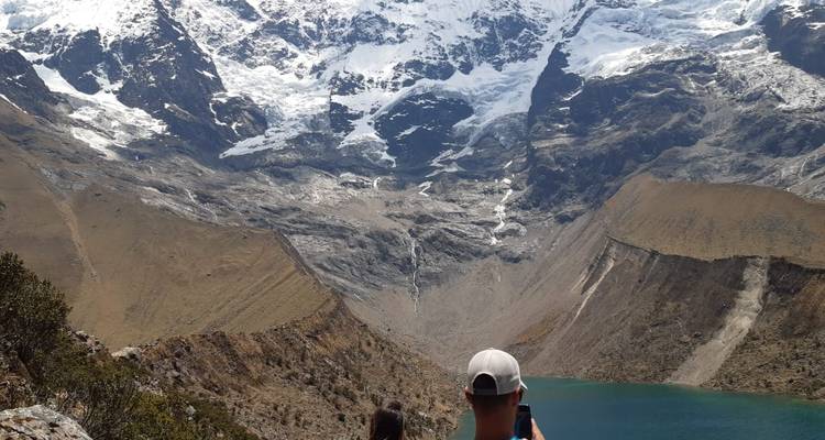 A person taking photos of a mountainous landscape with a lake.