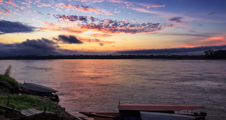 Atardecer sobre un río con barcos y nubes coloridas.