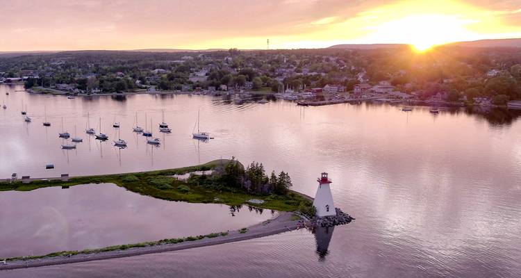 Vue aérienne d'un phare blanc sur une étroite langue de terre entourée d'eaux cristallines au coucher du soleil